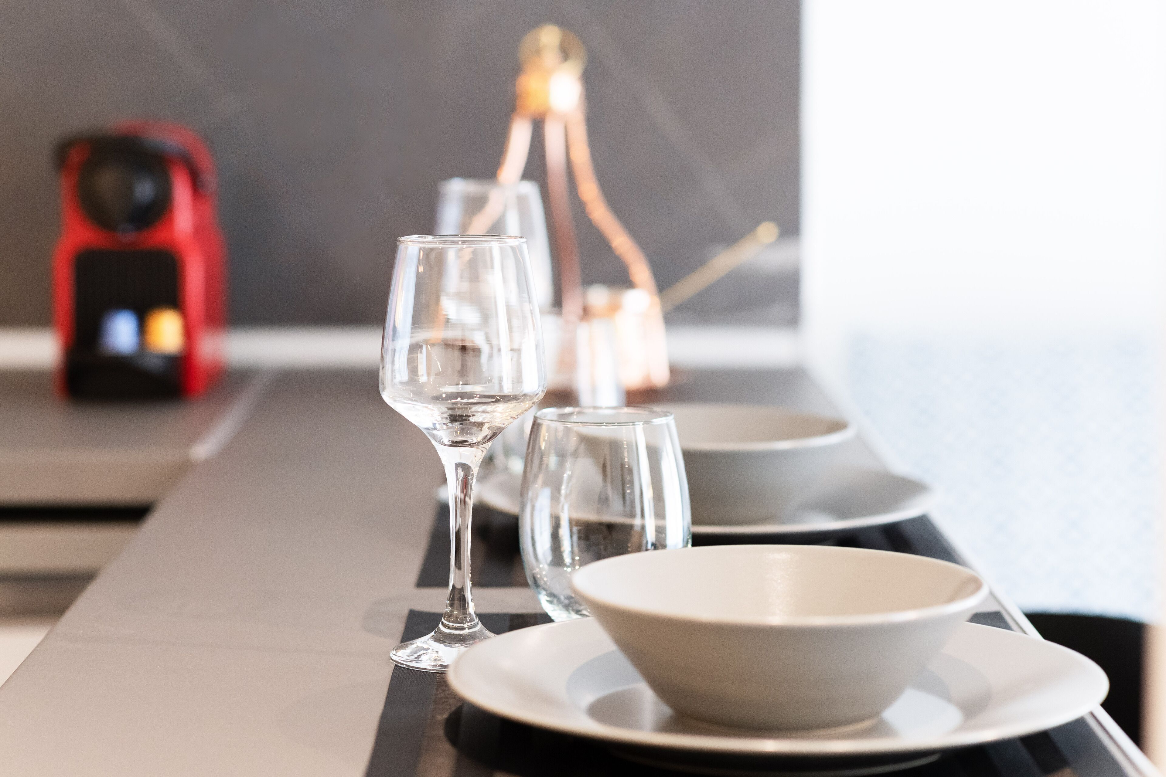 A dining table with clear glassware and plates, a red kettle, and a bottle of water.