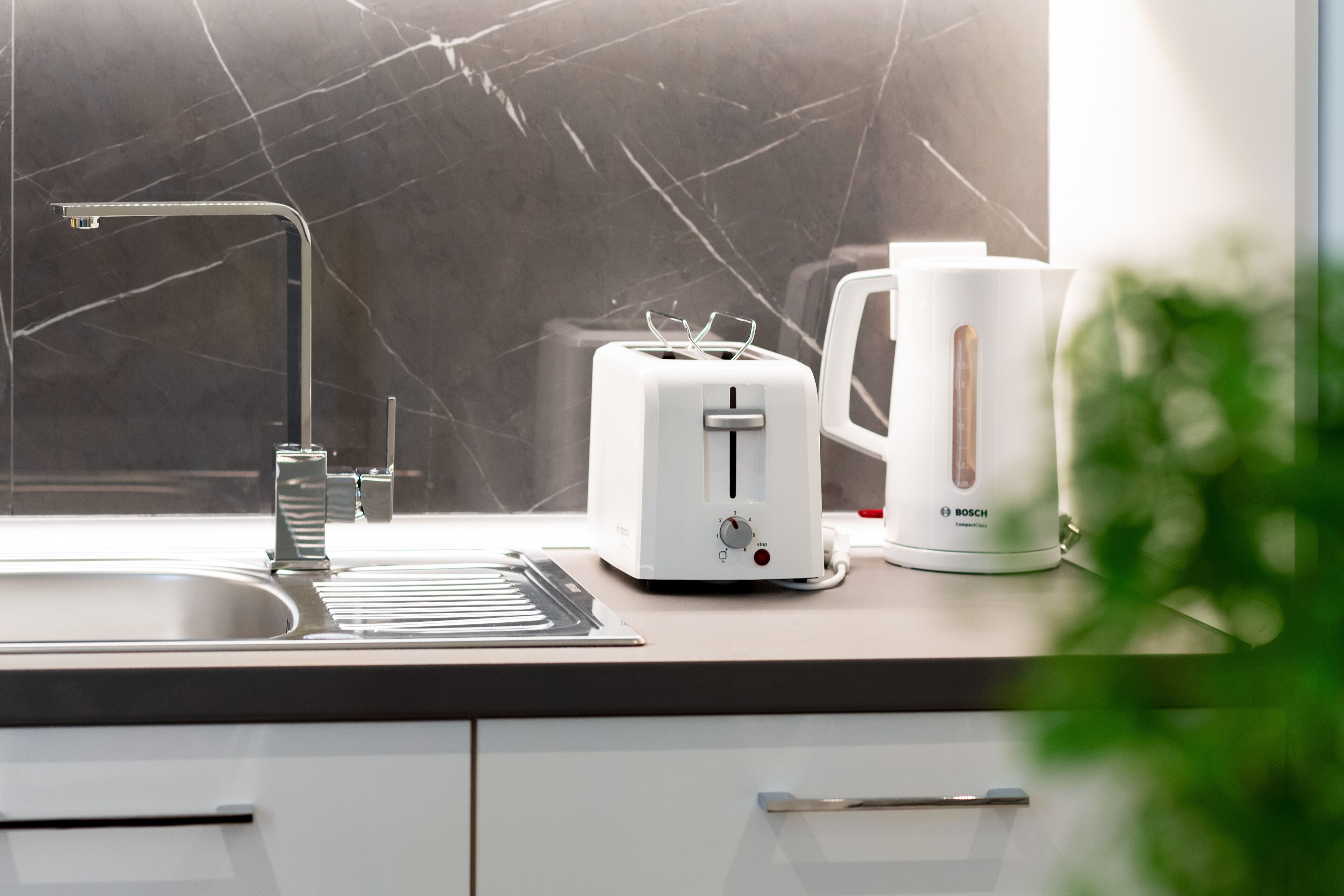 Een keuken met een modern design, met een Bosch broodrooster, een koffiezetapparaat en een gootsteen met een kraan.