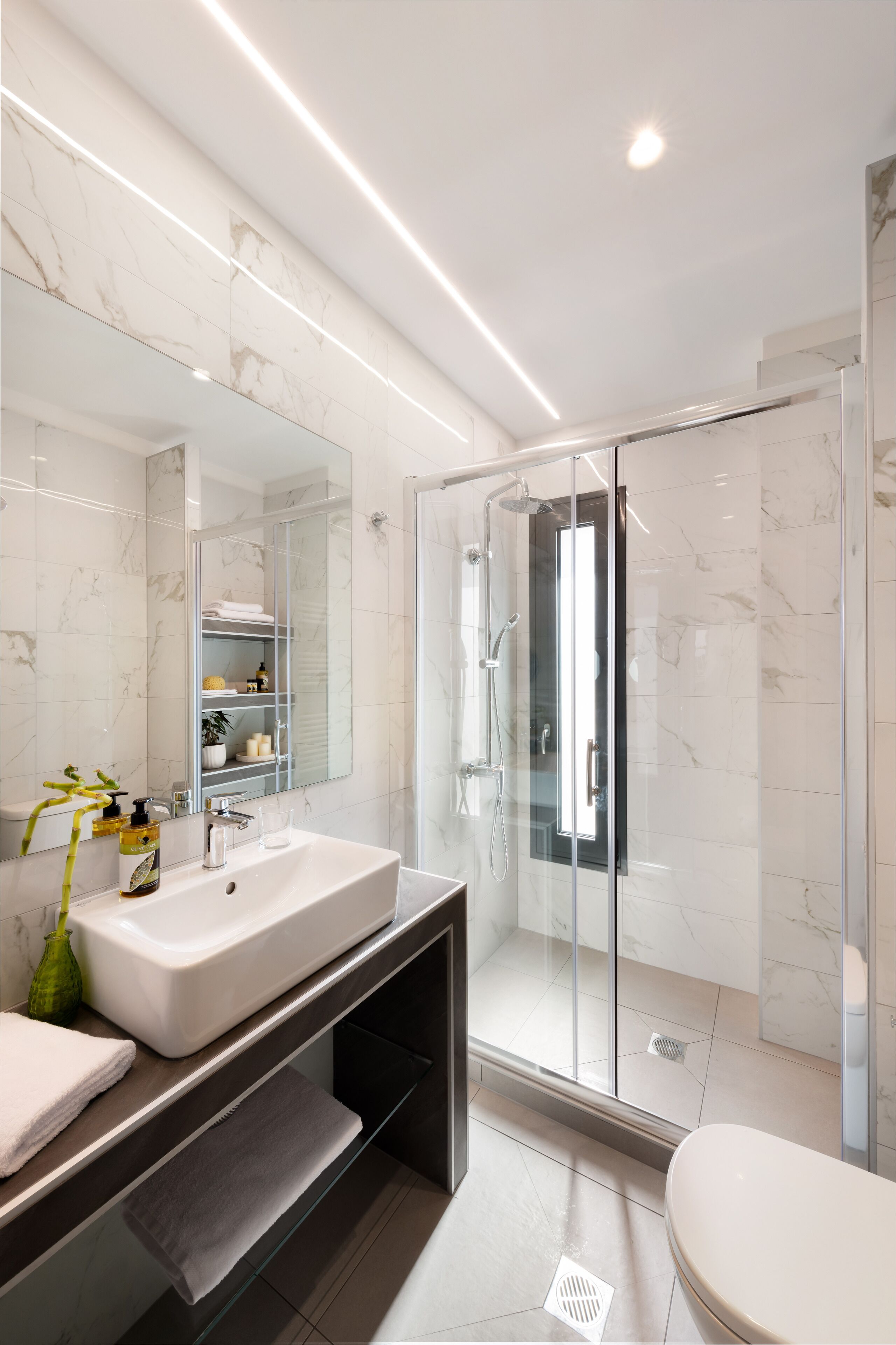 Un baño moderno con ducha envuelta en vidrio, un espejo grande y un lavamanos blanco.