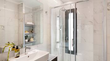 Un baño moderno con ducha envuelta en vidrio, un espejo grande y un lavamanos blanco.