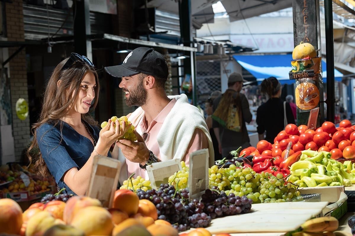 Un étal de marché proposant des produits frais, notamment des raisins, des tomates et des pommes.