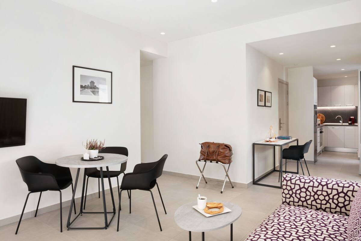 A modern living room with a dining area, a sofa, and a kitchen visible in the background.