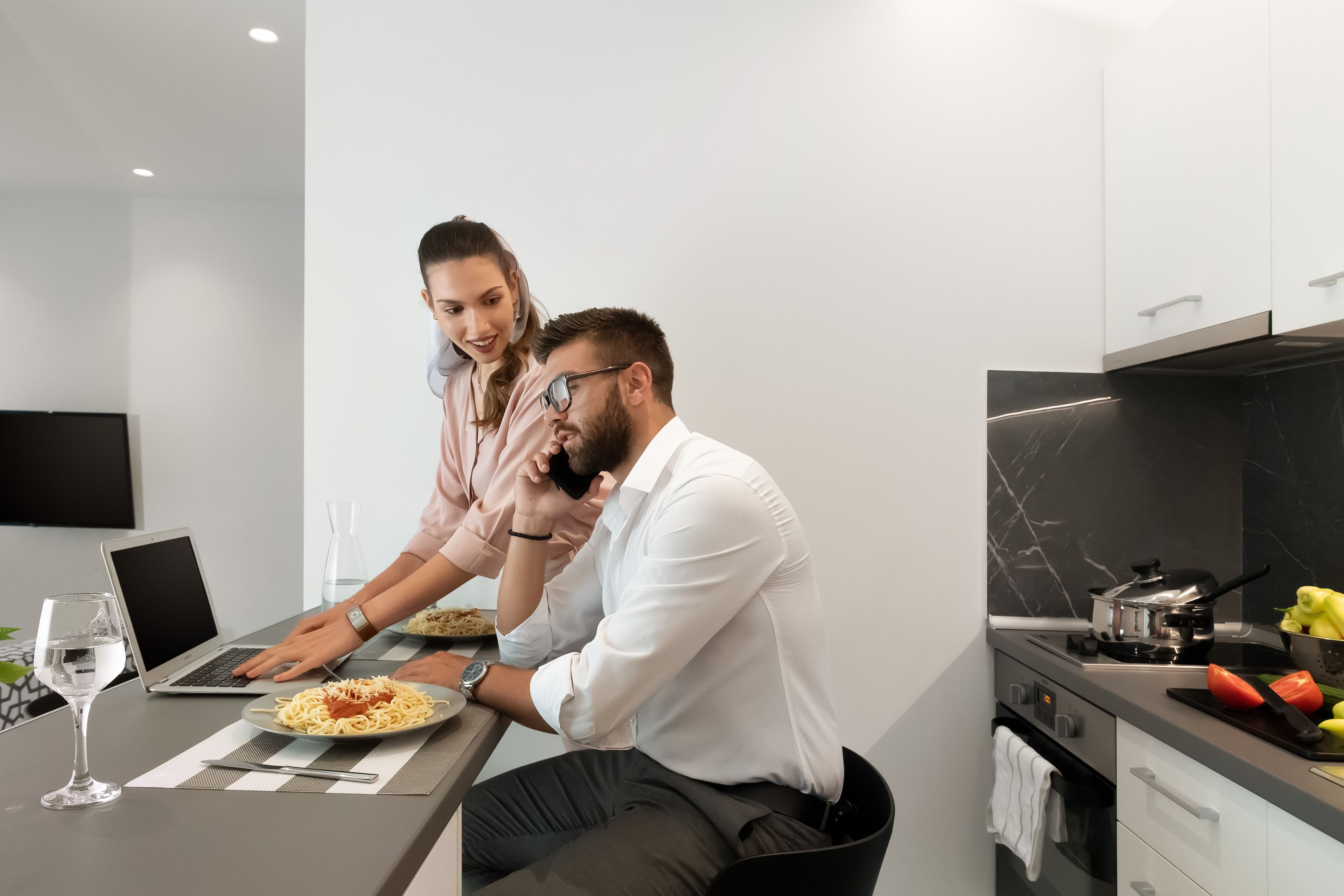 A modern kitchen with a dining table, laptop, and a glass of water.