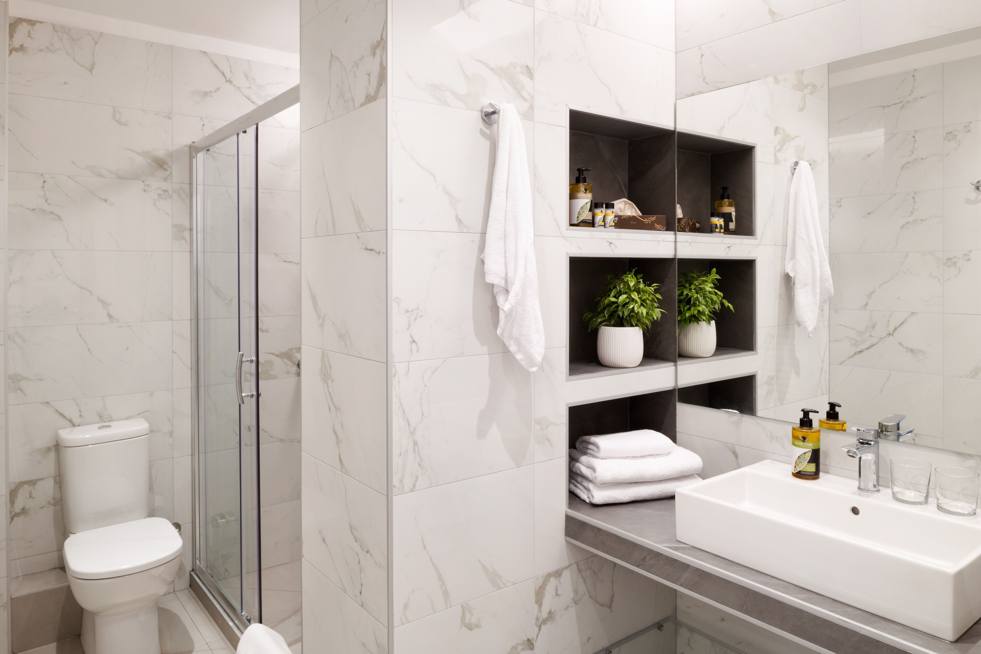 A modern bathroom with a glass shower enclosure, a white sink, and marble walls.