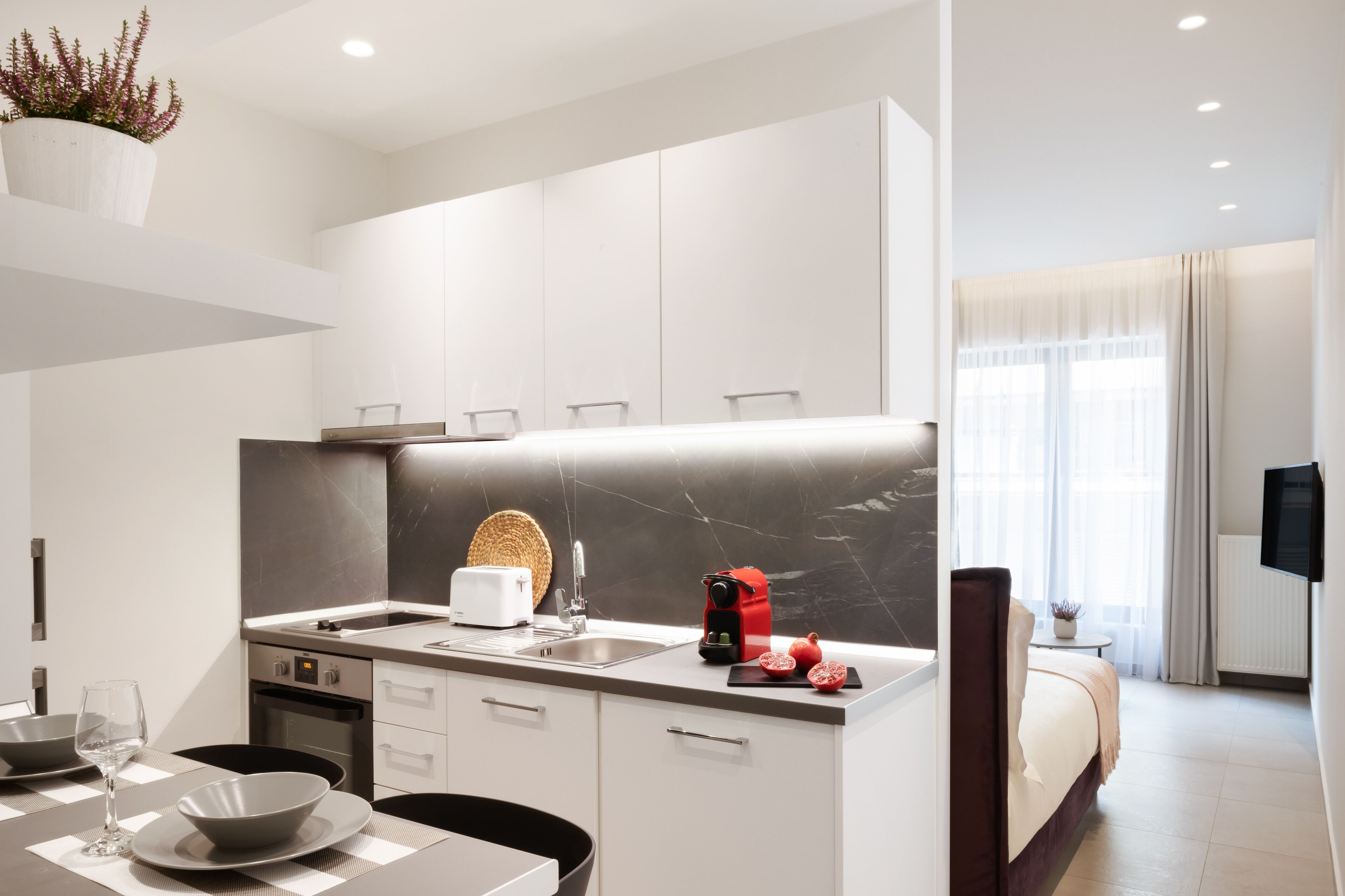 A modern kitchen with a marble backsplash, a built-in oven, and a coffee machine.