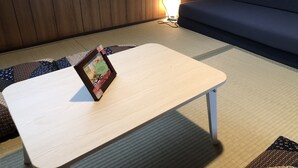 A room with a wooden floor, a light-colored table with a picture frame, a blue sofa, and a wall-mounted fire extinguisher.