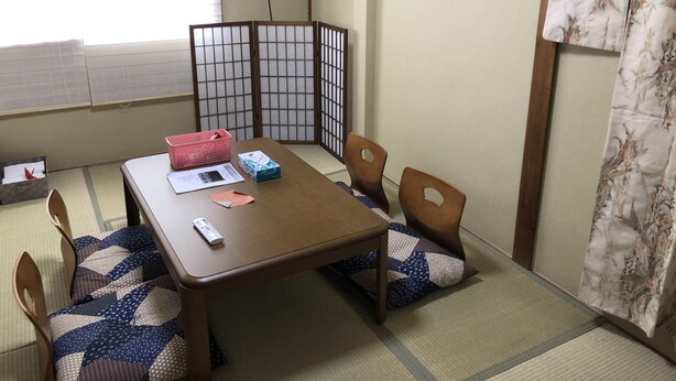 A traditional Japanese room with tatami flooring, a low table, wooden chairs, a shoji screen, and a futon bed.