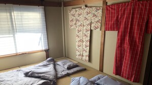 A traditional Japanese room with tatami flooring, a futon bed, a shoji screen, and a red striped curtain.