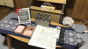 A hotel reception desk with a welcome sign, a guest check-in list, a remote control, and a patterned cushion.