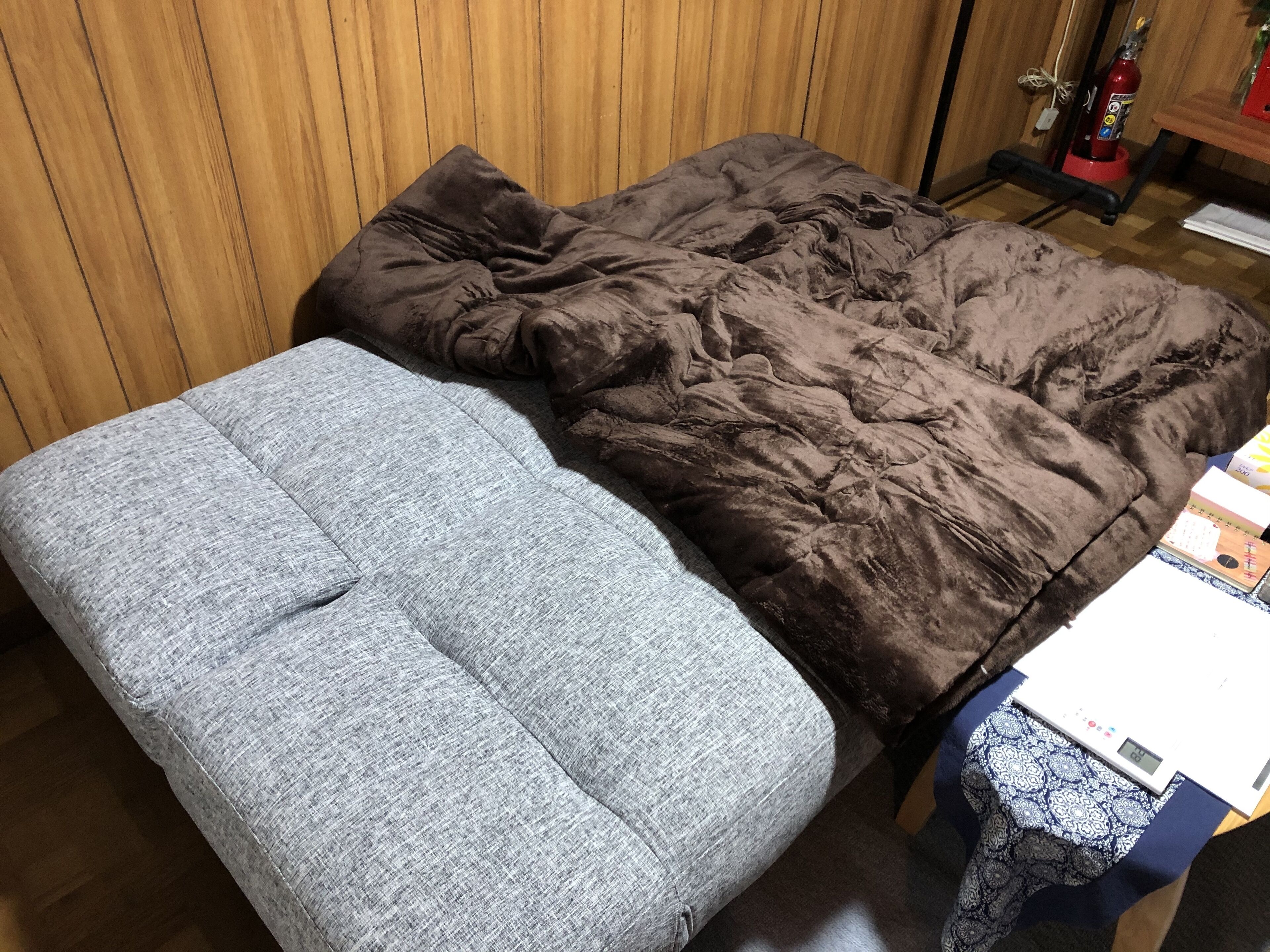 Una habitación con una cama, una mesita con una balanza y un extintor.
