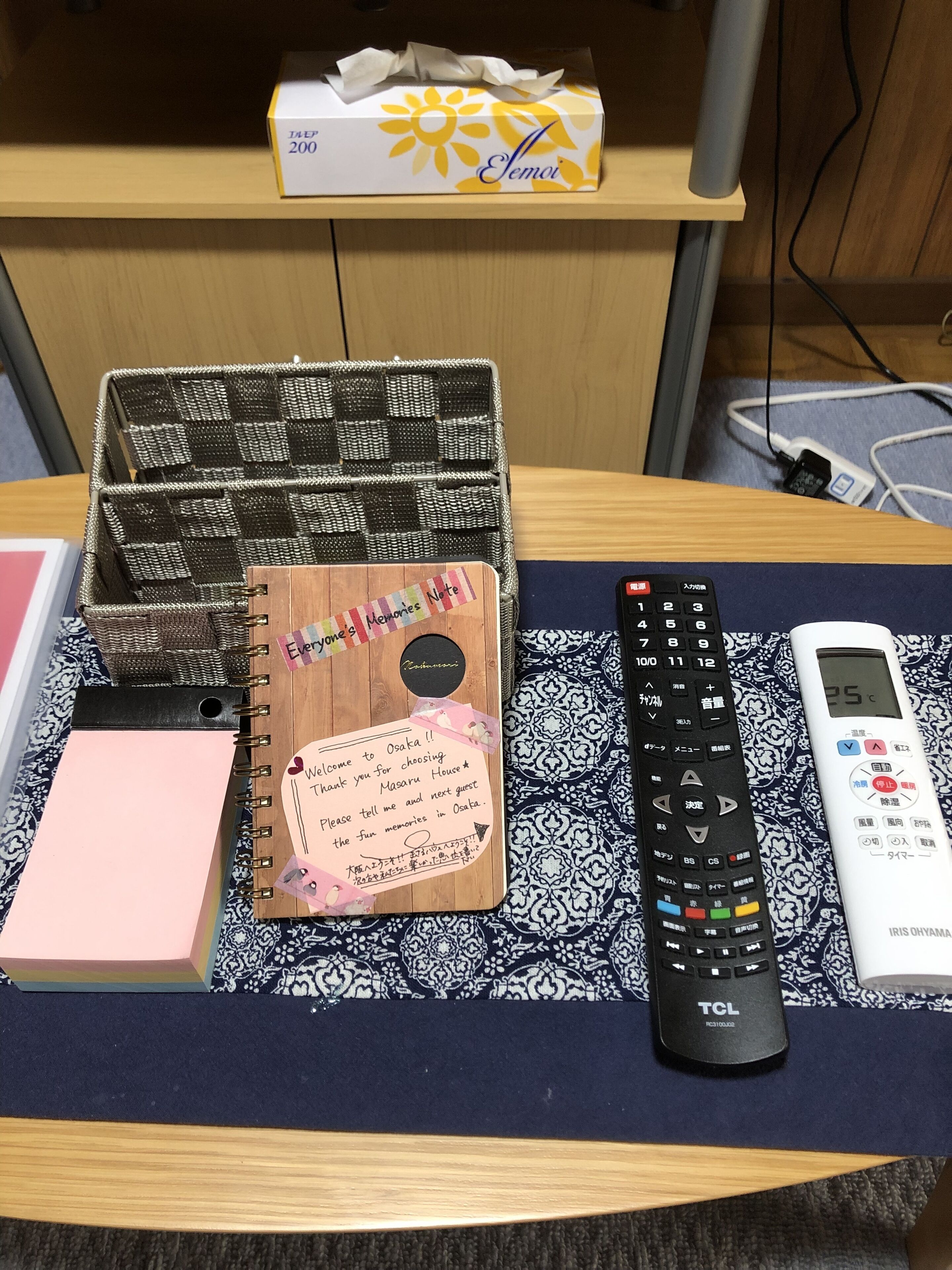 A desk with a notebook, a remote control, a pen, and a tissue box.