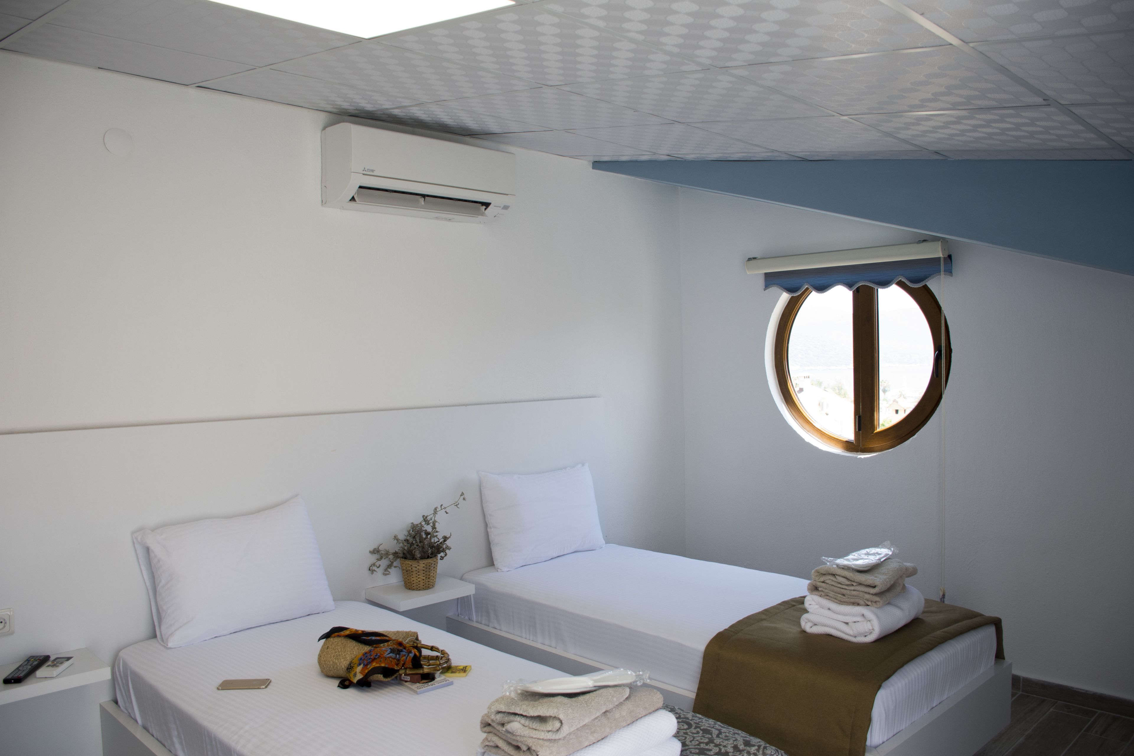 A hotel room with a bed, a bedside table, a window, and an air conditioning unit.