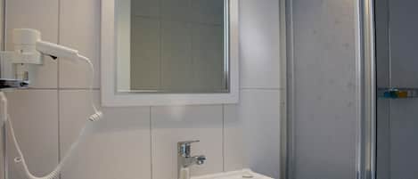 A bathroom with a white sink, a mirror, and a hairdryer on the wall.
