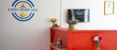 Un mostrador de recepción con un logotipo, un televisor y un certificado enmarcado en la pared.