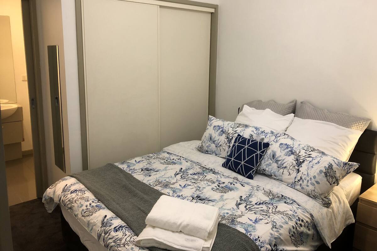 Un dormitorio con cama, almohadas, una manta, una mesita de noche y un armario.