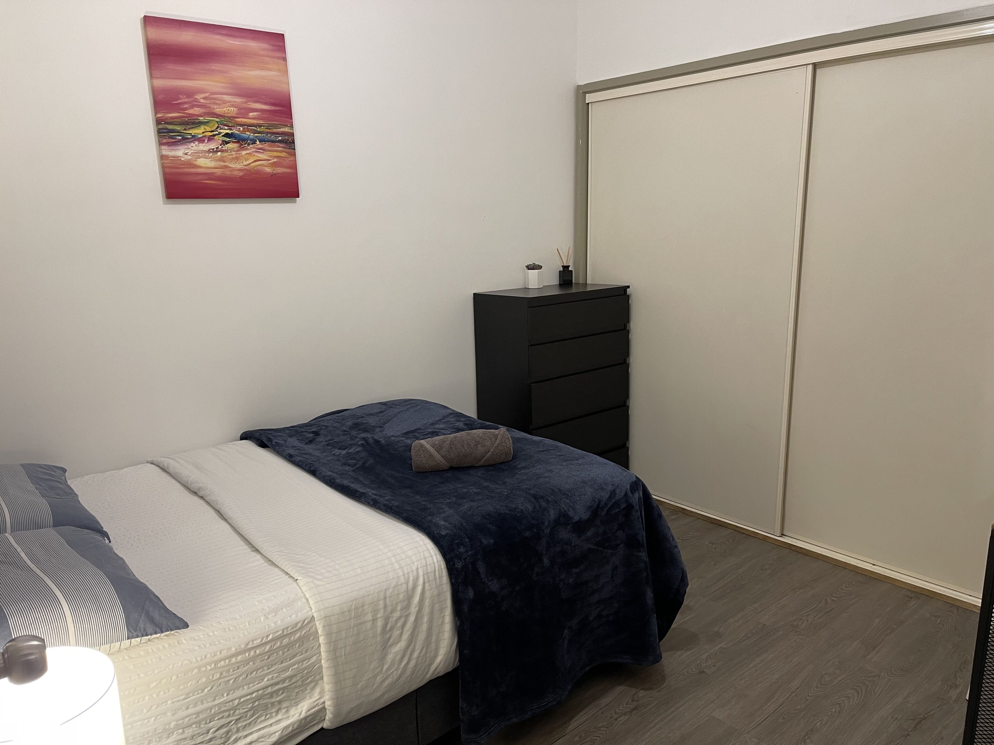 A bedroom with a bed, a dresser, a closet, and a painting on the wall.
