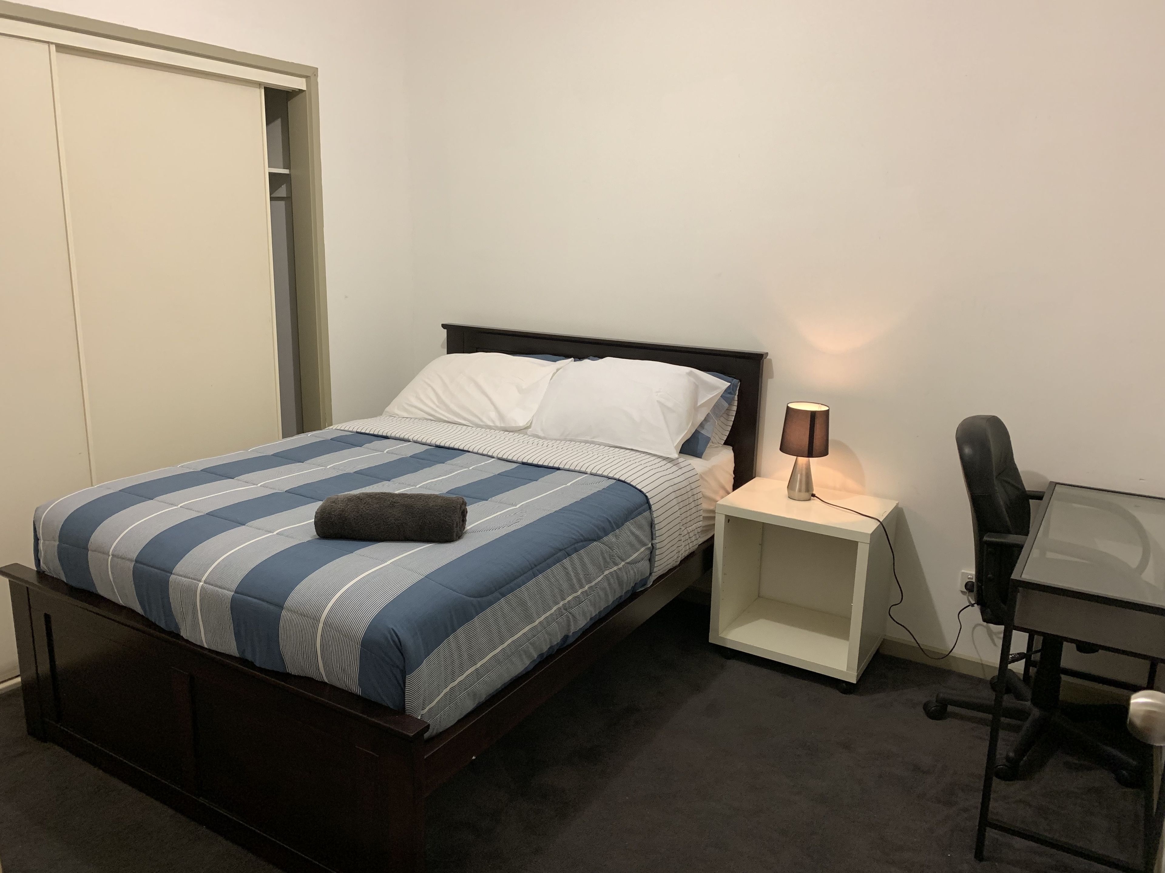 Ein Schlafzimmer mit einem Bett, einem Nachttisch mit Lampe, einem Schreibtisch mit Stuhl und einem Kleiderschrank.