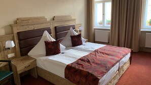 A double bed with a floral bedspread, two nightstands with lamps, a wooden headboard, and a window with curtains. - Goldner Löwe (Stolpen)