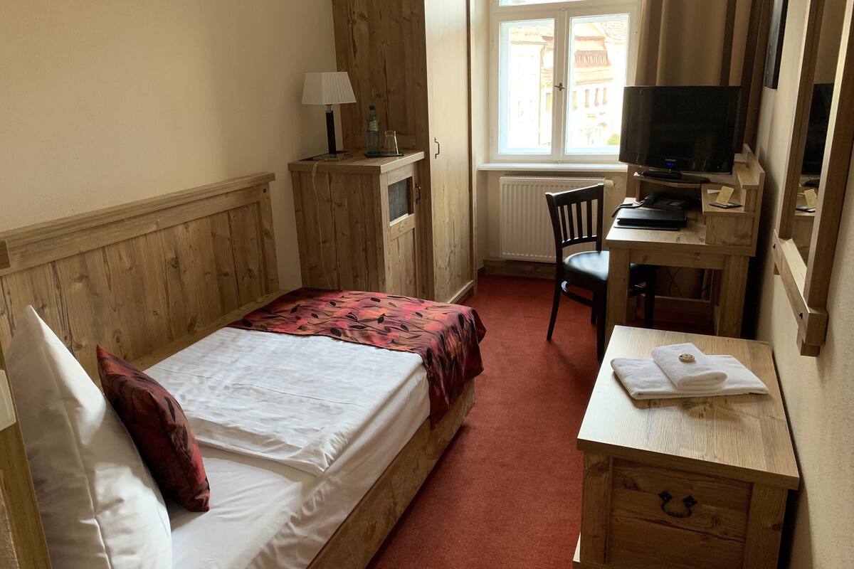 A hotel room with a bed, a desk with a chair, a television, and a window with curtains.