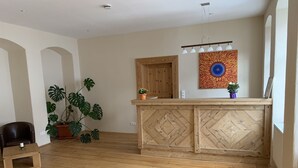 A room with a wooden floor, a wooden reception desk, a potted plant, a chair, and a wall with a colorful artwork. - Goldner Löwe (Stolpen)