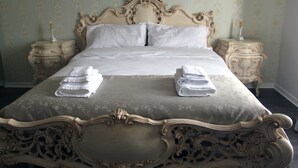 Een groot, decoratief bed met een bloemenbedekking en twee nachtkastjes met kaarsen.