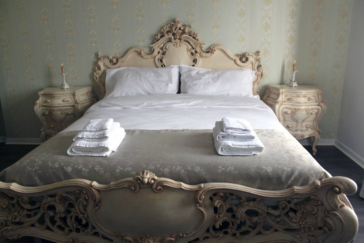 Un grand lit somptueux, agrémenté d’une couvre-lit à motifs floraux et flanqué de deux tables de chevet sur lesquelles sont posées des bougies.