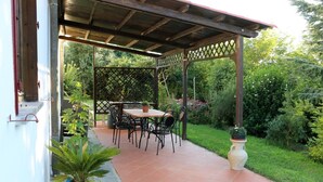 Een overdekte patio met een tafel en stoelen, omgeven door weelderige beplanting en een potplant.