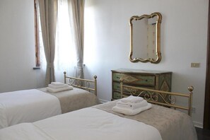 Une chambre avec deux lits simples, une commode, un miroir et une fenêtre avec des rideaux.