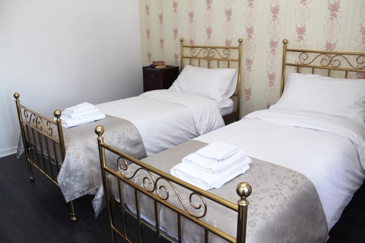 Two single beds with metal frames and white bedding, a small bedside table, and floral wallpaper.