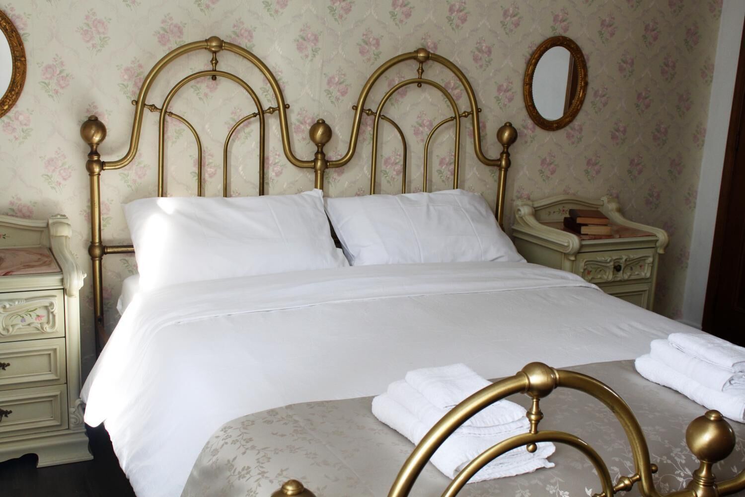 Un lit bien fait, avec une tête de lit dorée, du linge de lit blanc et un papier peint à motifs floraux.