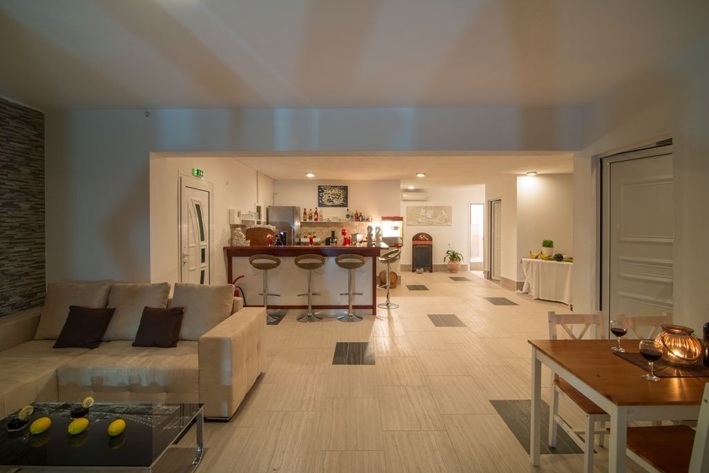 Un salon moderne comprenant un canapé, une table basse et un coin repas avec une table et des chaises. On aperçoit à l’arrière un coin cuisine avec un bar et des tabourets.