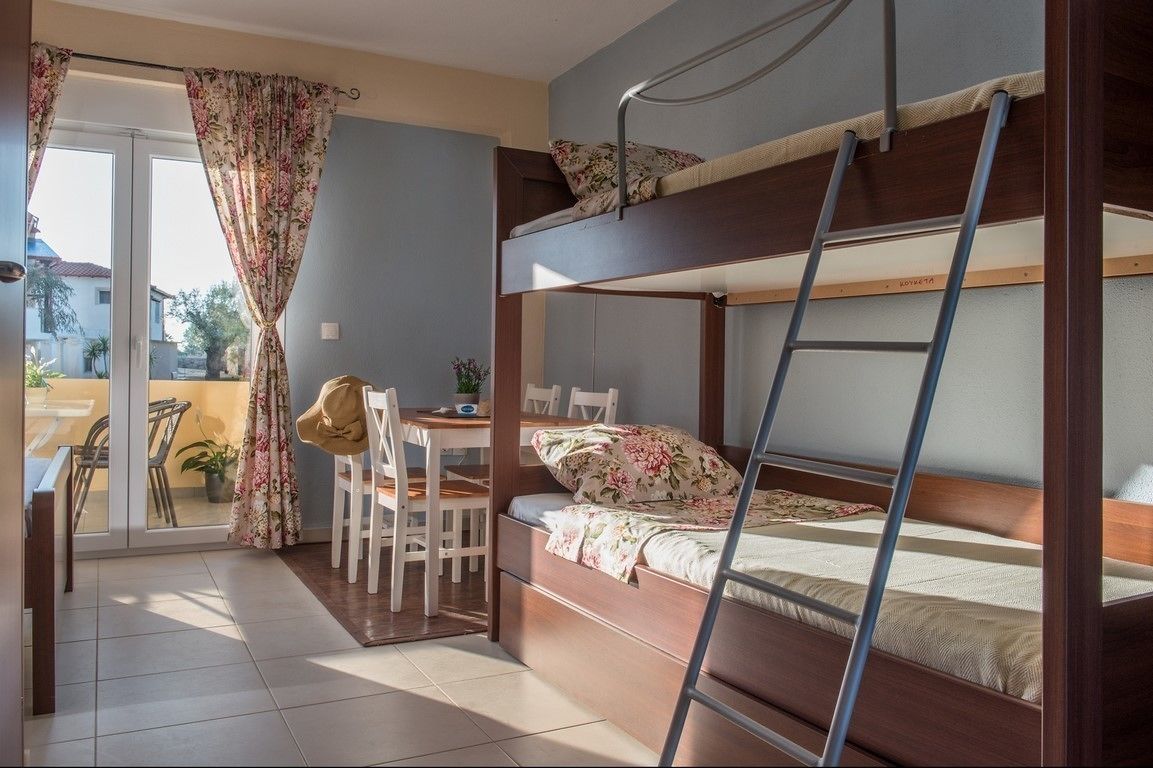 A bunk bed room with a desk and chair, a ladder, and a view of the outside.