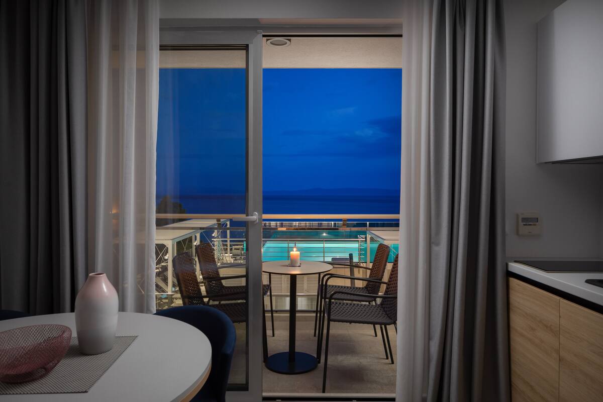 Ein Balkon mit Blick auf das Meer, ein Tisch mit Stühlen, eine Vase und eine Kerze.