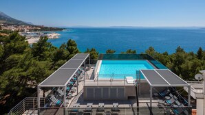 Une piscine sur le toit, avec une eau d’un bleu limpide, entourée de chaises longues et offrant une vue sur la mer et les montagnes lointaines.