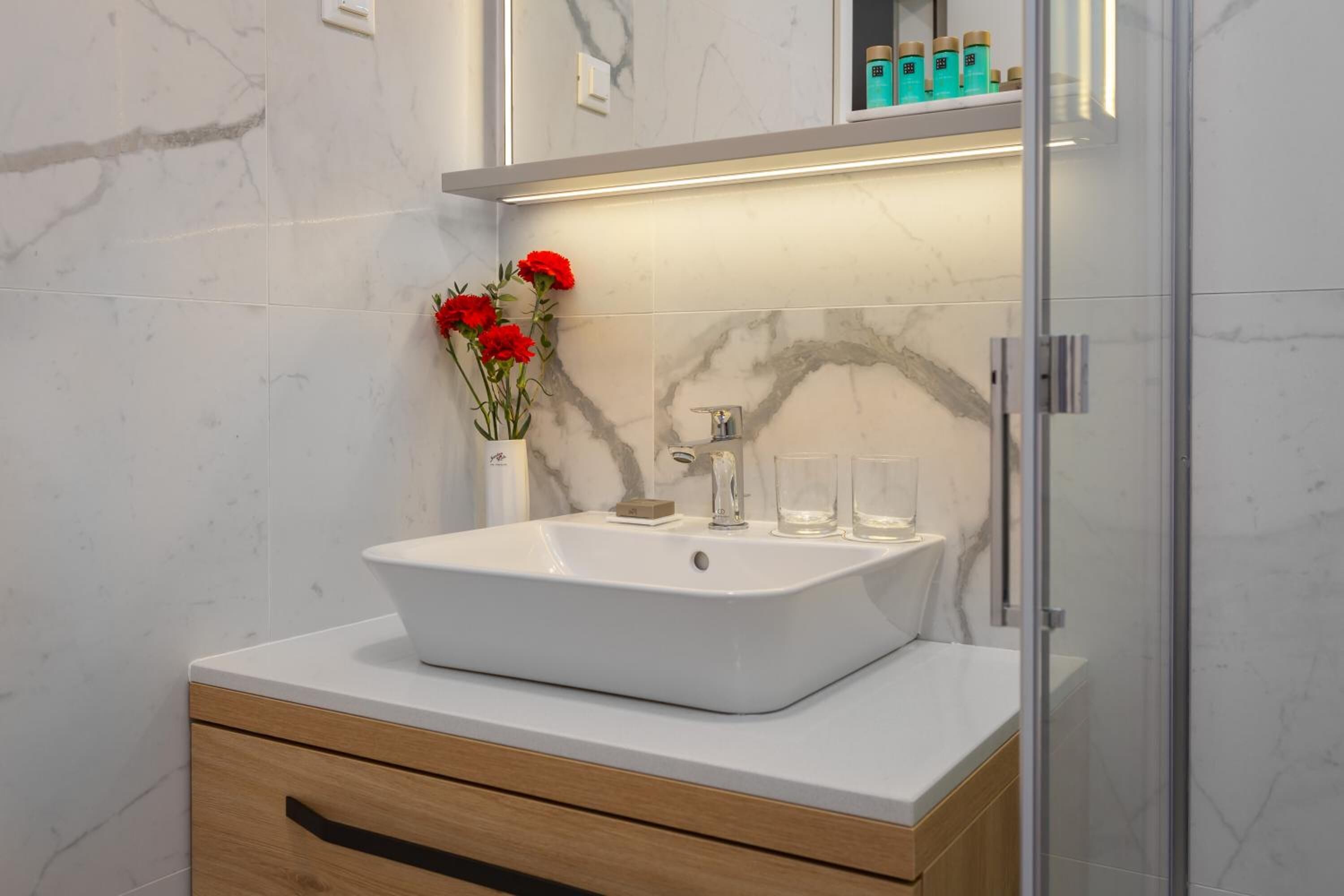 A bathroom with a white sink, marble tiles, a wooden cabinet, and a glass shower enclosure.
