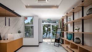 Un espace d’accueil moderne avec un sol en marbre, un comptoir d’accueil en bois et une porte vitrée donnant sur l’extérieur.