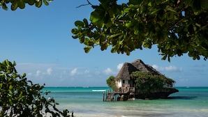 A thatched-roof hut with a wooden deck, surrounded by clear turquoise waters and lush greenery. - Upendo Beach Boutique Hotel (Michamvi)