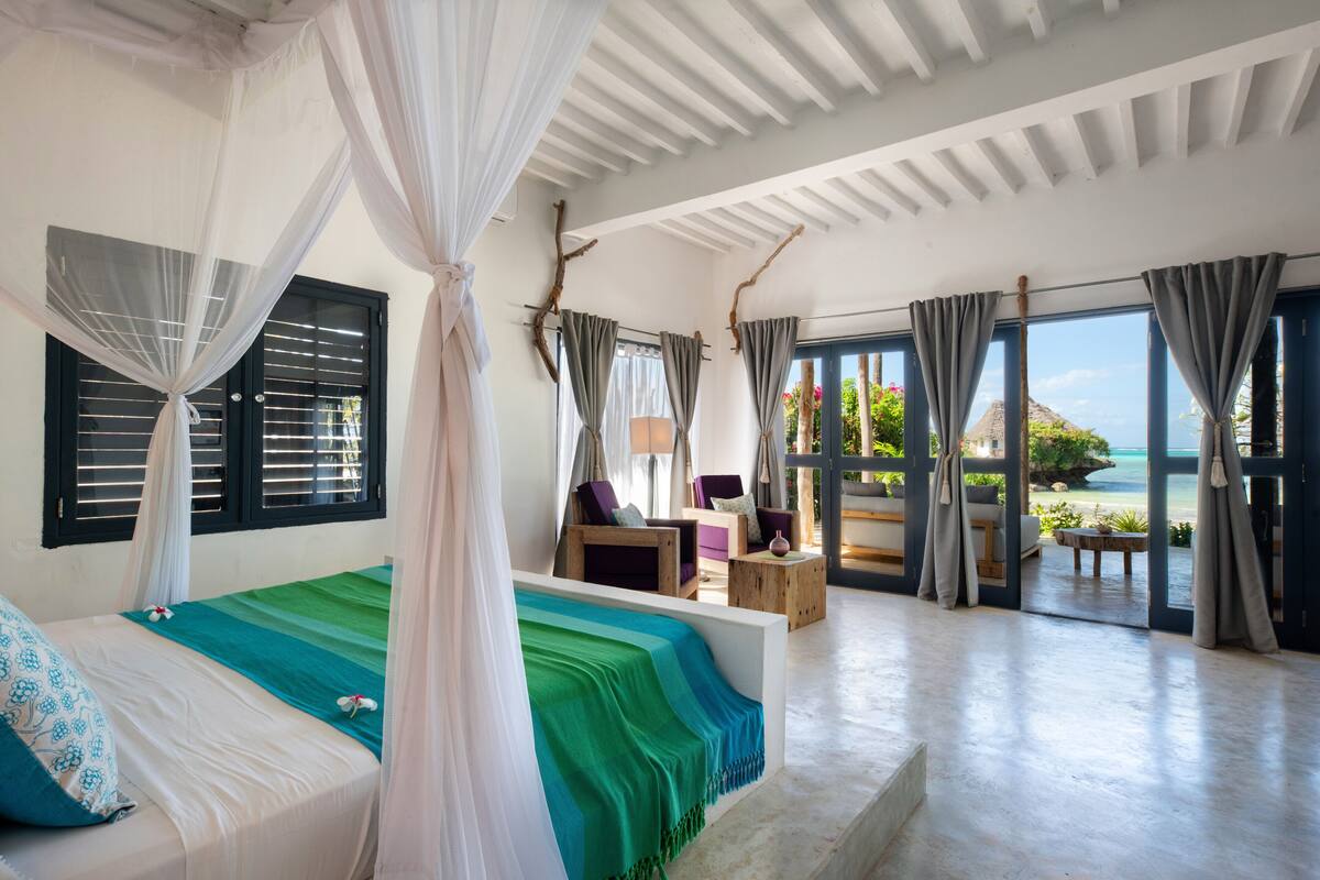 Ein geräumiges Zimmer mit einem Bett, einer Sitzecke mit Sesseln und großen Fenstern mit Meerblick.