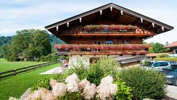 Eine traditionelle Holzhütte mit Balkon, geschmückt mit Blumen, umgeben von üppigem Grün und blauem Himmel.