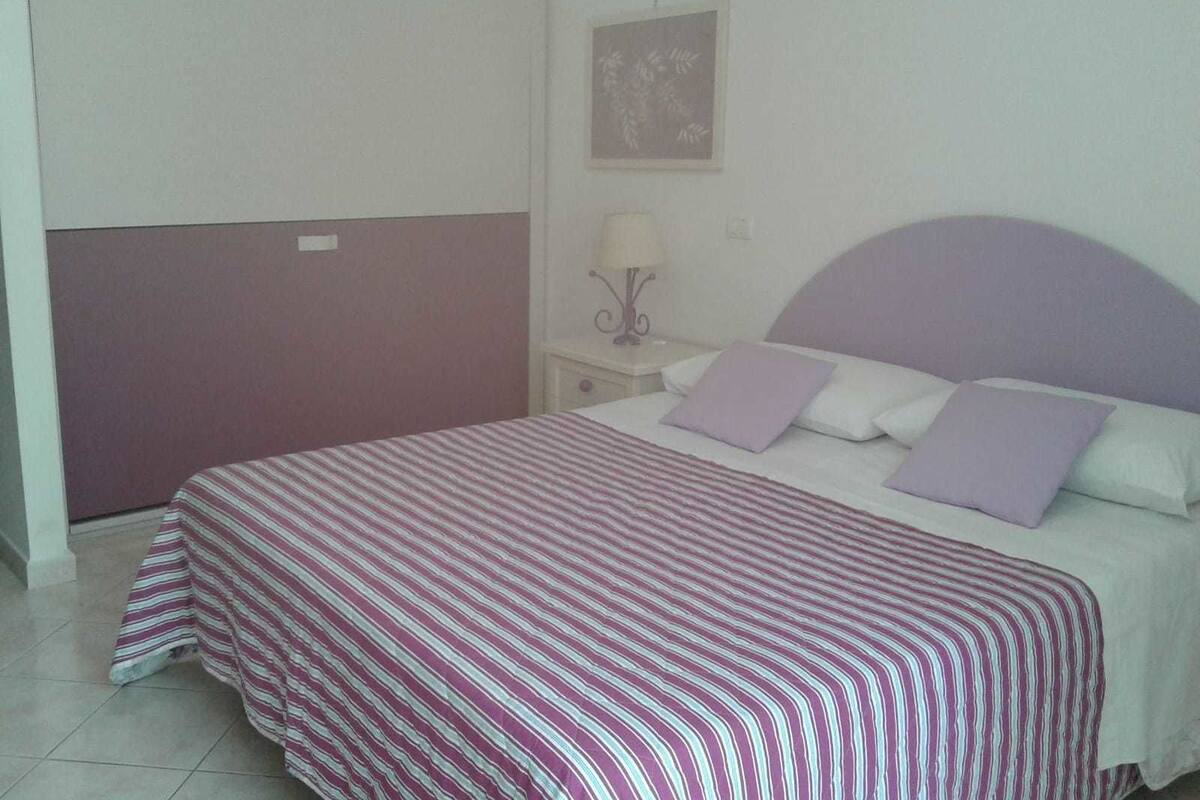A bedroom with a bed, a nightstand, a lamp, and a framed picture on the wall.