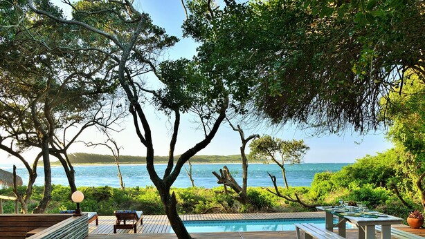 A wooden deck with a pool, lounge chairs, and a table with a view of the sea. - Cabo Beach Villas (Machangulo)