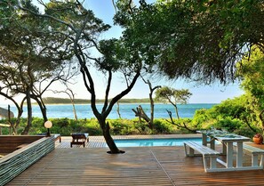 Una terraza de madera con piscina, sillas de descanso y una mesa con vistas al mar.