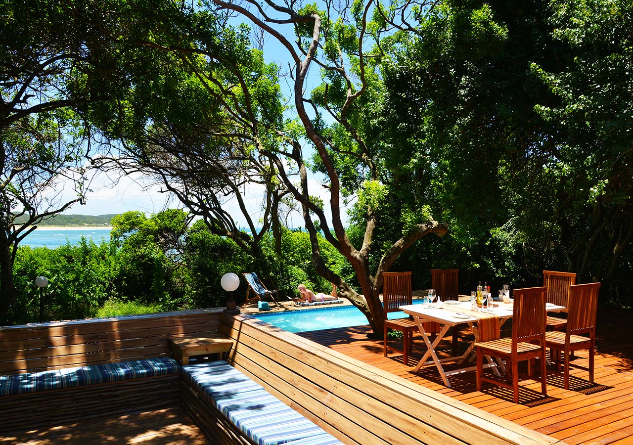 A wooden deck with a pool, outdoor seating, and a table with chairs.