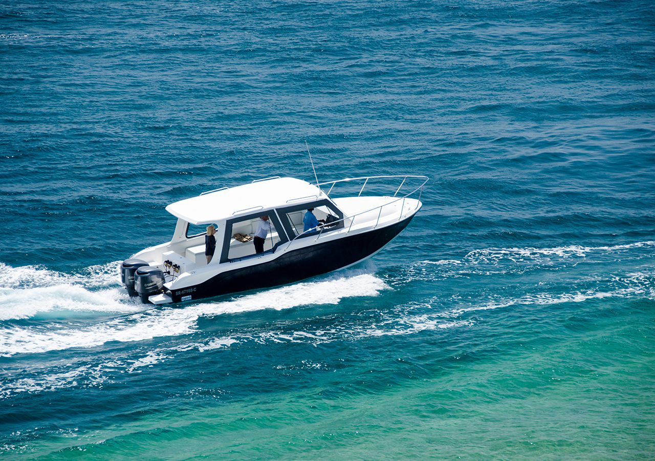 Un petit bateau à moteur blanc, doté d’une cabine et ne laissant apercevoir qu’une seule personne à bord, qui se déplace sur une eau d’un bleu limpide.