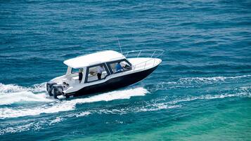 Un petit bateau à moteur blanc, doté d’une cabine et ne laissant apercevoir qu’une seule personne à bord, qui se déplace sur une eau d’un bleu limpide.