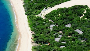 An aerial view of a beach resort with a clear beach, dense greenery, and a small pool area. - Cabo Beach Villas (Machangulo)