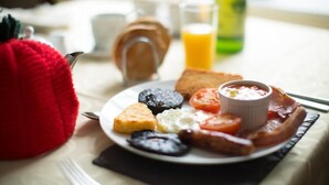 A breakfast plate with toast, eggs, tomatoes, and bacon on a table with a red bag and a glass of orange juice in the background. - Hardwick Farm (Abergavenny)