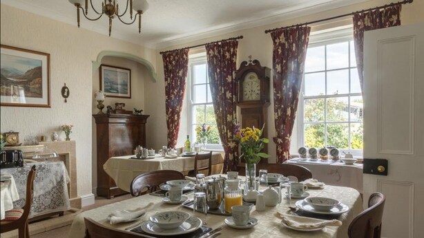 A dining room with a table set for breakfast, a clock, and a view of the outdoors. - Hardwick Farm (Abergavenny)