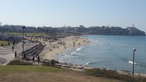 A coastal cityscape with a wide beach, promenade, and urban buildings in the background. - Sea Front Penthouse (Tel Aviv)