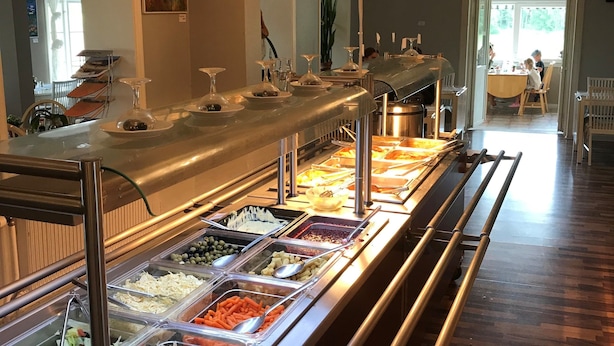A buffet area with various food options, a chandelier, and a dining area in the background. - Finspångs Golfklubbs Stugby (Finspang)